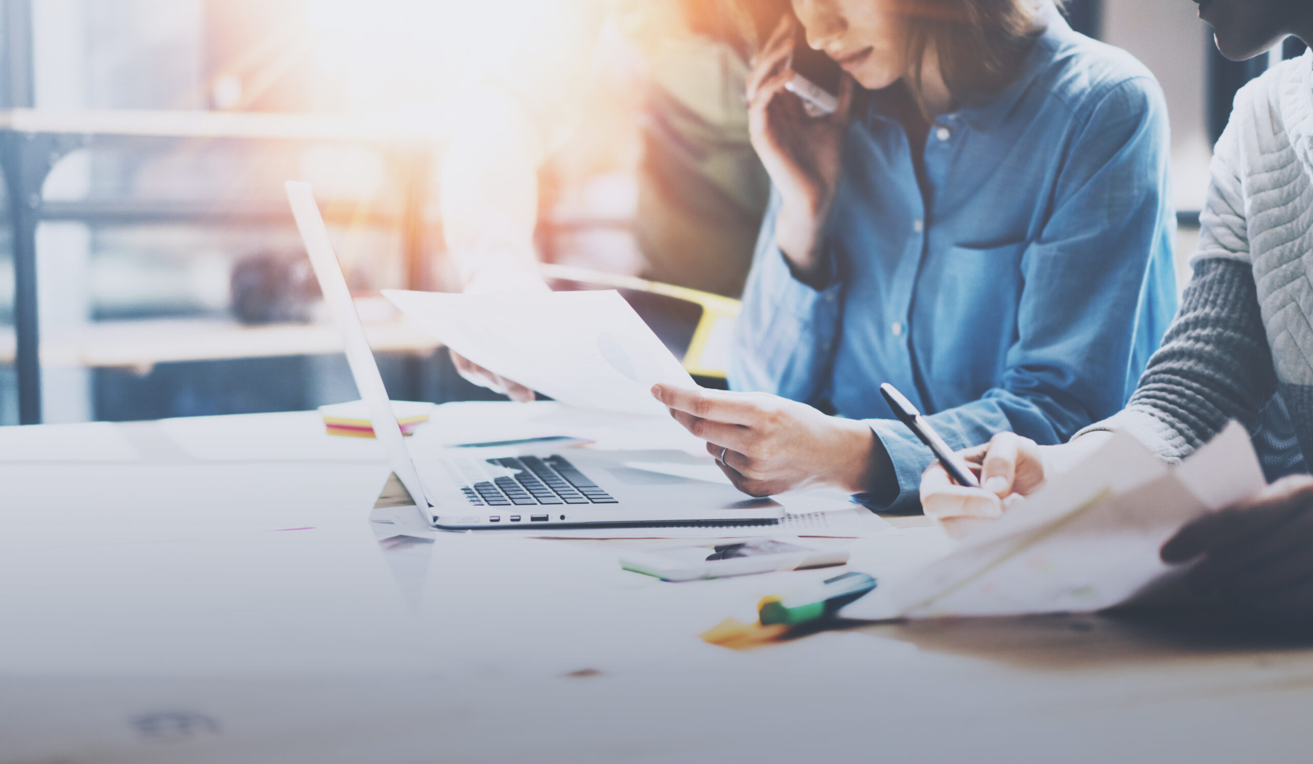 Teamwork process concept.Young coworkers working with new startup project at the office.Girl holding paper document in hand and using smartphone.Horizontal, blurred background